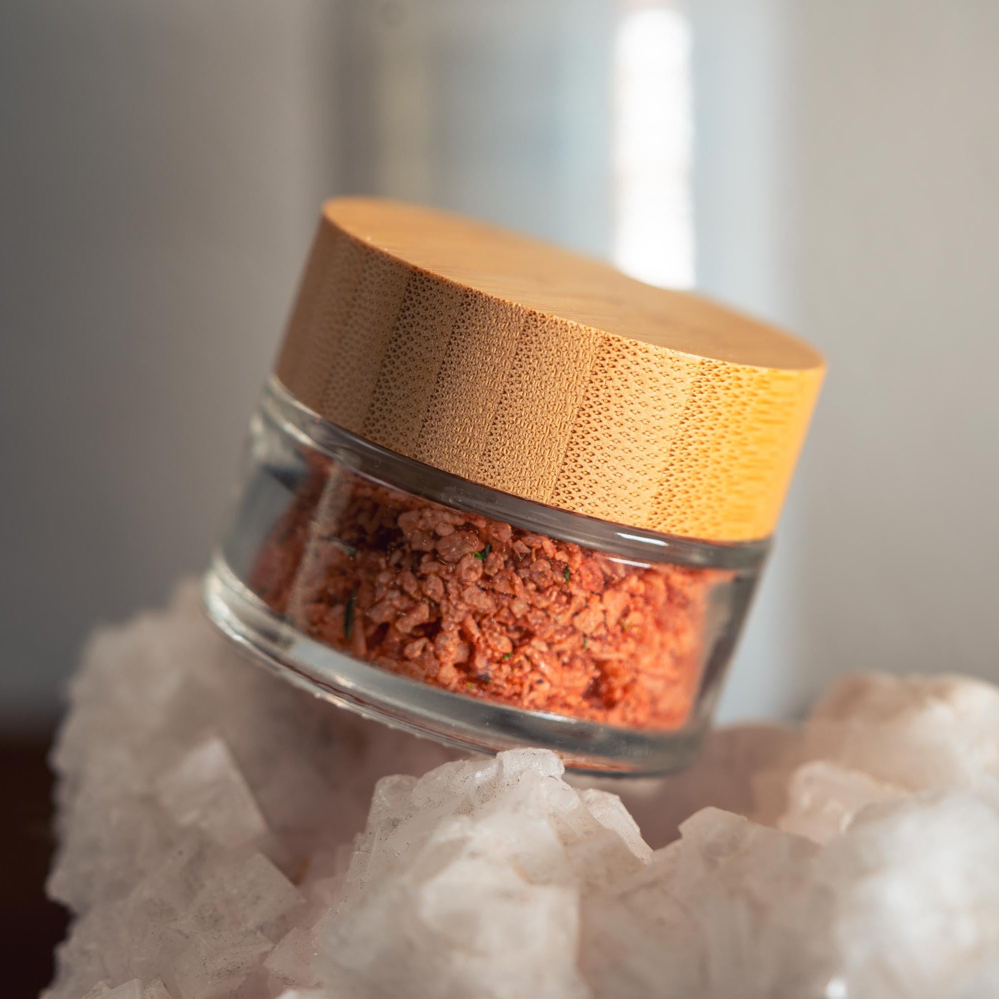 Glass jar with wooden lid containing a red spice on a white rock
