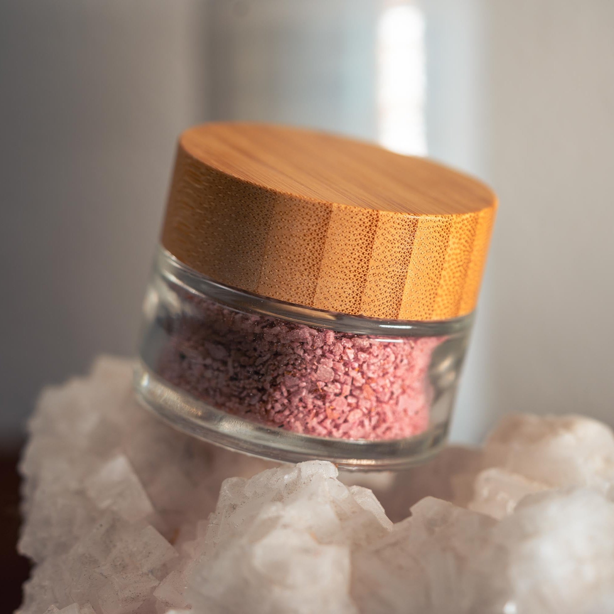 Small glass jar with pink contents on a white rock against a neutral background