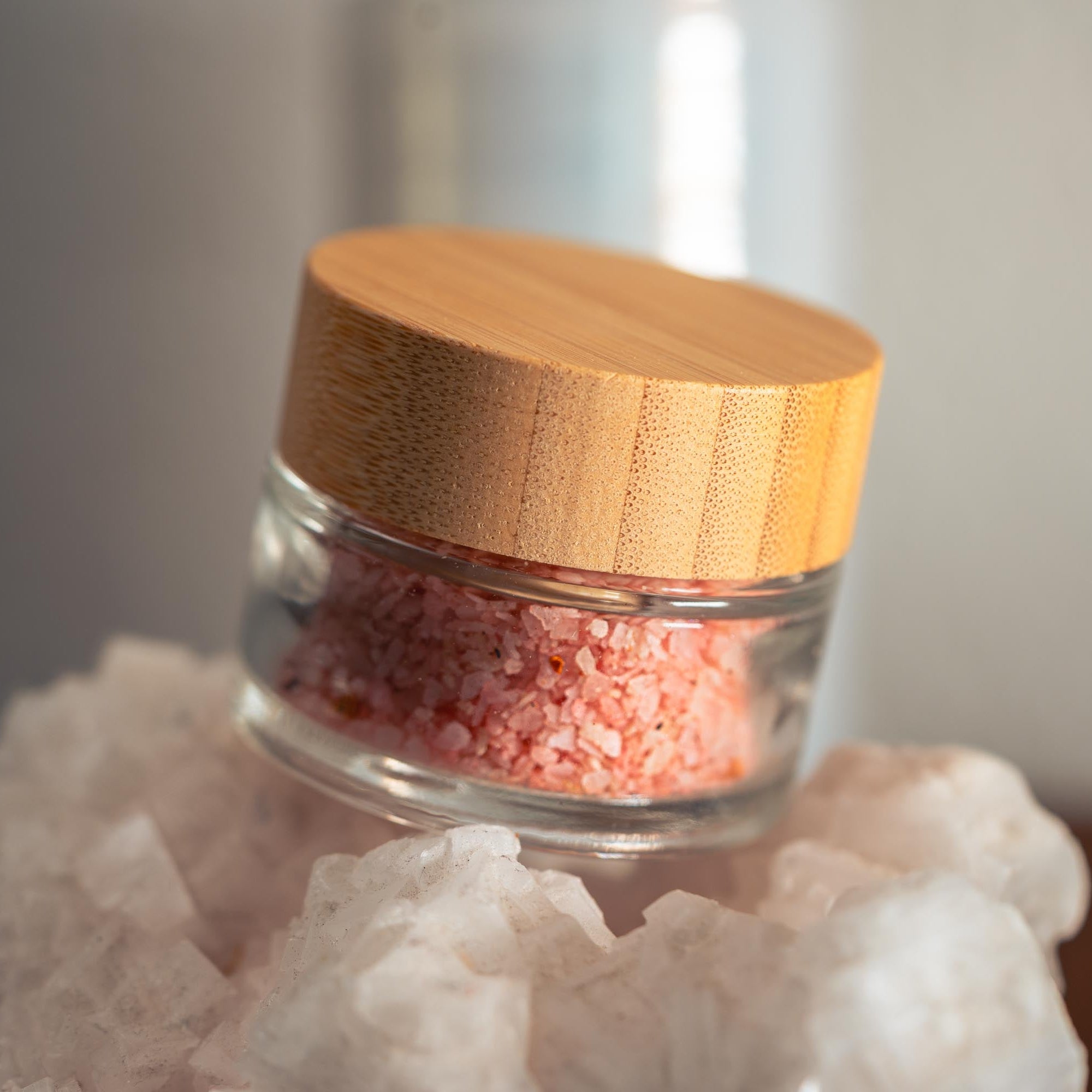 Glass jar with pink salt on a white rock with a wooden lid.